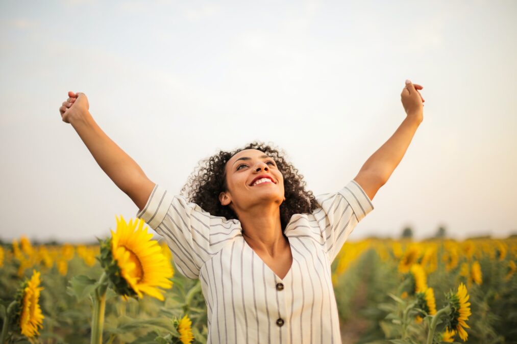 Chica en un campo de girasoles con los brazos estirados