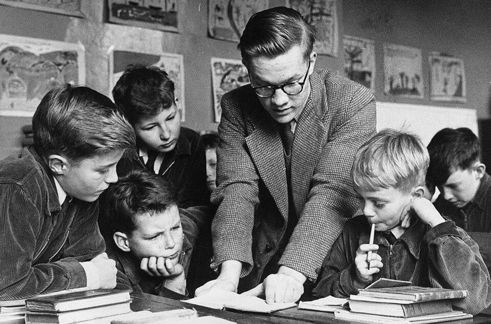 Un profesor señala un libro mientras los alumnos le escuchan. Estudiar. Escuela. Alumno. Profesor