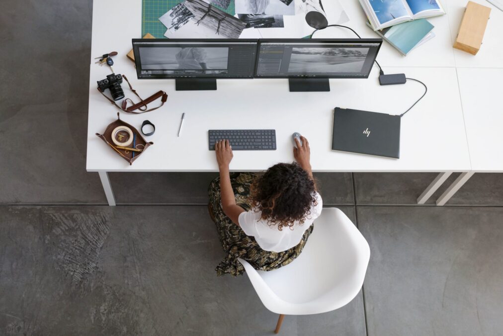 HP - Una chica delante de dos pantallas de ordenador con un portátil a su izquierda
