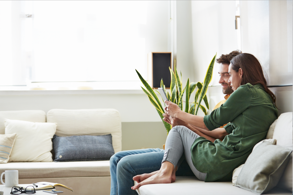 Una pareja sentados en el sofá de su salón miran su tablet