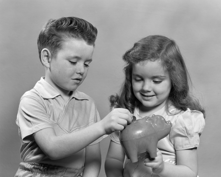 Niño y niña echan dinero en una hucha de cerdito