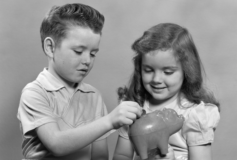 Niño y niña echan dinero en una hucha de cerdito