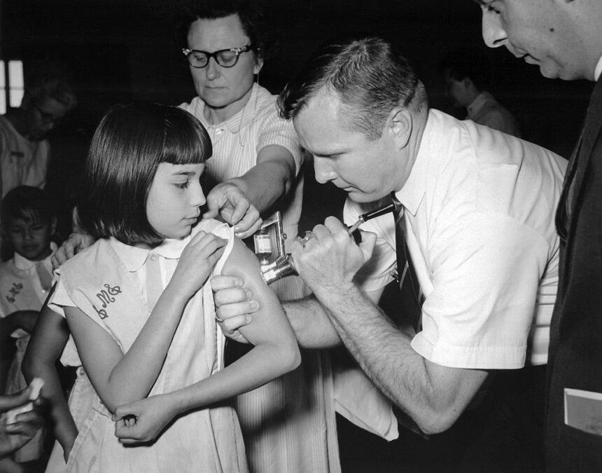 Un señor pincha en el brazo una aguja a una niña